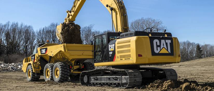 CAT digger dumps dirt into yellow dump truck using custom machined parts for earth moving equipment by Lange Grinding and Machining near Cleveland